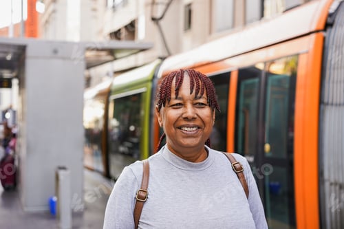 Preview: Mature african woman smiling in front of camera at tram station in the city