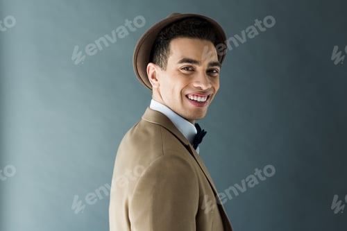 Preview: stylish mixed race man in suit looking at camera and smiling isolated on grey