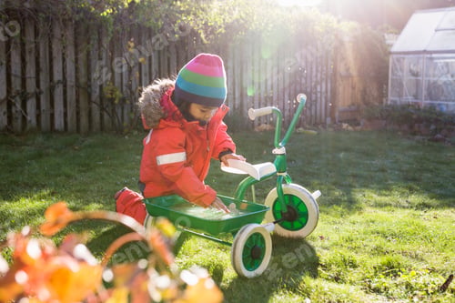 Preview: Girl (4-5) with tricycle in garden