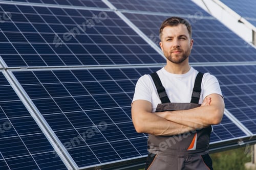 Preview: A portrait of a confident bearded male engineer, arms crossed, standing before solar panels