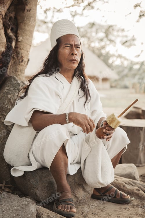 Preview: Portrait of an Arhuaco indigenous dressed in his traditional dress sitting on the roots of a tree.