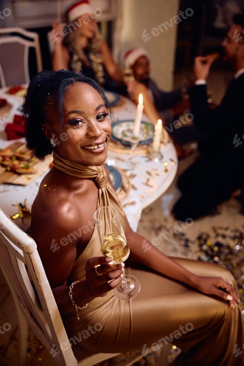 Preview: Happy black woman having a glass of champagne on Christmas party and looking at camera.