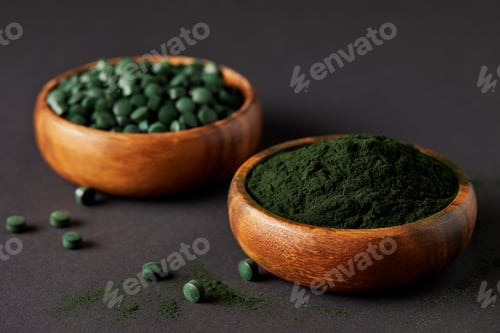 Preview: selective focus of wooden bowls with ground spirulina and spirulina in pills on grey table