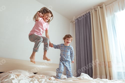 Vista previa: Actividad positiva en interiores. Niños pequeños saltando sobre una cama y divirtiéndose