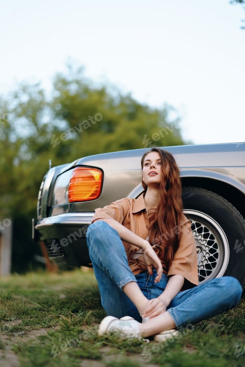 Preview: Young woman sitting beside a vintage car, wearing casual fashion and expressing contemplation in a