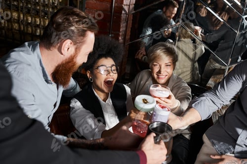 Preview: excited african american woman clinking glasses with multiethnic workmates in bar after work