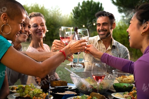 Preview: Diverse happy friends toasting with wine and beer during garden dinner party. Friends having fun.