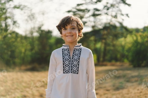 Preview: A boy smiles confidently while standing in a sunlit field, wearing a traditional embroidered shirt