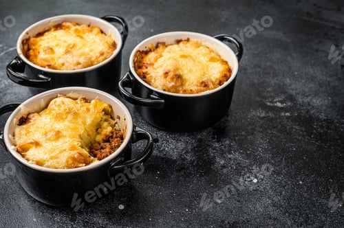Preview: Homemade shepherd's pie with ground meat, mashed potato and cheddar cheese crust. Black background.