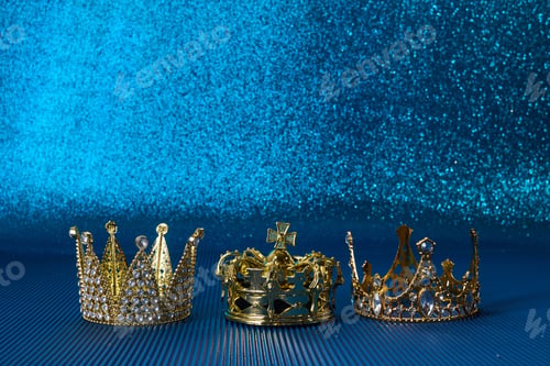 Preview: Epiphany Day or Dia de Reyes Magos concept. Three gold crowns on blue sparkling background