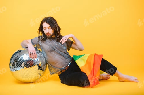 Preview: gay man with a gay pride flag smiling and looking away on yellow background.