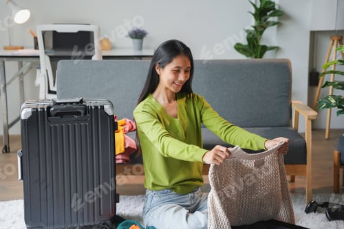 Preview: Young woman is packing her suitcase in the living room, preparing for an upcoming trip
