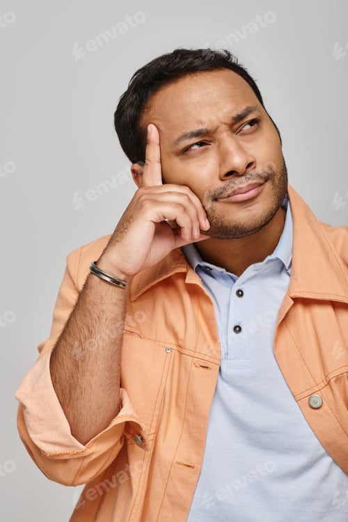 Preview: focused indian man in bright orange jacket posing actively and looking away on gray backdrop