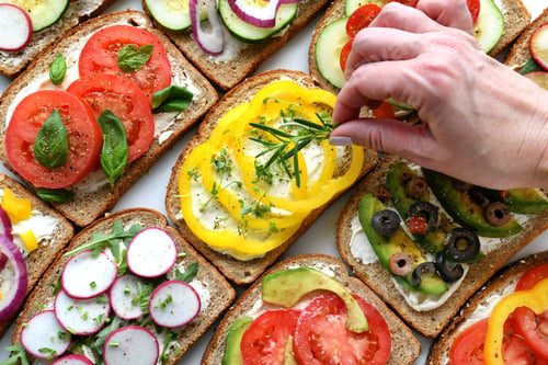 Preview: Female adding garnish to open face vegetable sandwiches - vegan vegetarian - colorful food flat lay