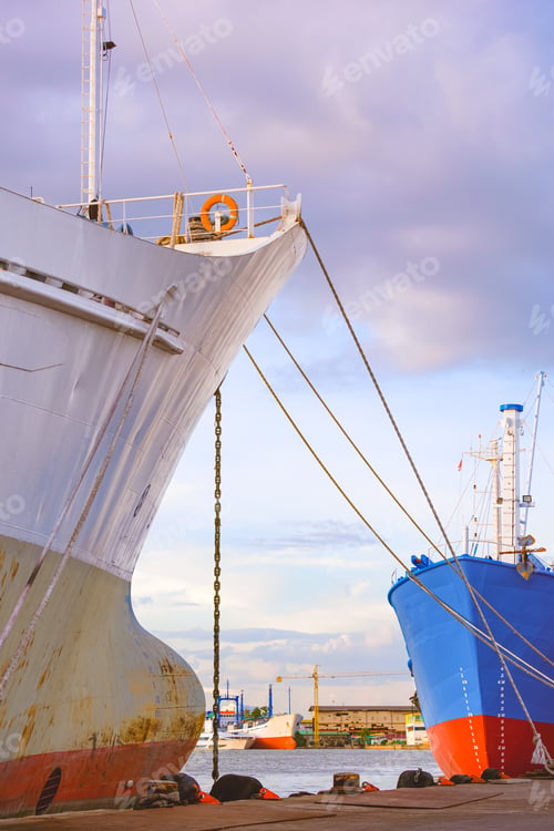 Preview: Part of oil tanker and fishing boat moored at harbor against cloudy sky in vertical frame