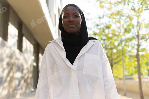 Preview: From below happy African American young confident businesswoman in black headscarf looking away