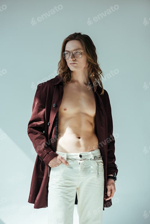Preview: fashionable shirtless man in glasses posing in trench coat, on grey