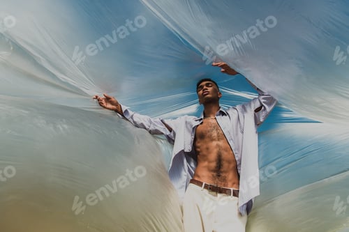 Preview: trendy african american man with closed eyes posing under polyethylene outdoors