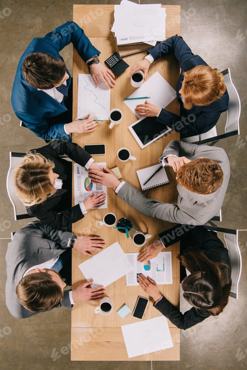 Preview: Top view of businesspeople discussing at table with digital devices, coffee cups and documents