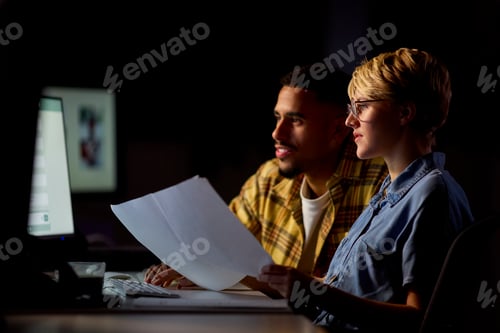 Preview: Two Business Colleagues At Desks In Office Working Late On Project Together