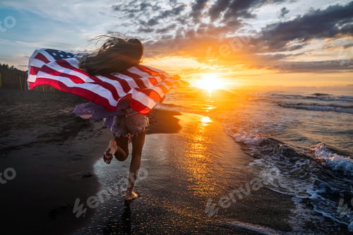 Preview: Young woman holding national American flag walking ocean beach. America Independence Day concept