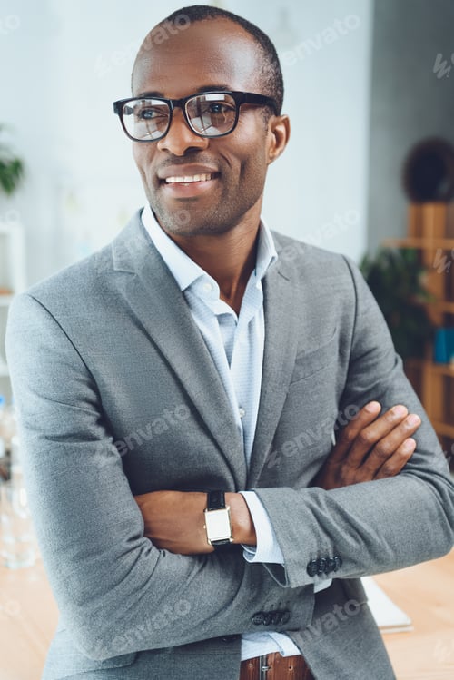 Preview: smiling african man with arms crossed looking away at office space