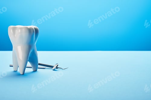 Preview: close up view of sterile dental mirror, probe and tooth model arranged on blue backdrop