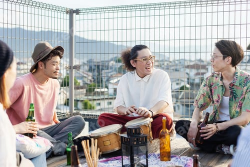 Preview: Group of young Japanese men and women sitting on a rooftop in an urban setting, drinking beer.