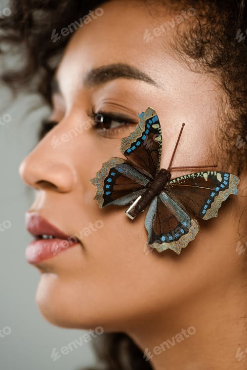Preview: close up of pretty african american woman with butterfly on face isolated on grey