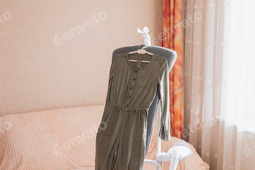 Preview: A dark green jumpsuit for a girl is prepared and hangs for vertical steaming on a white hanger.