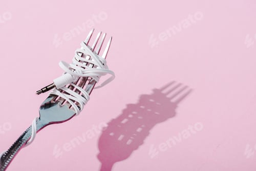 Preview: earphones wrapped over metal fork on pink with copy space, music concept