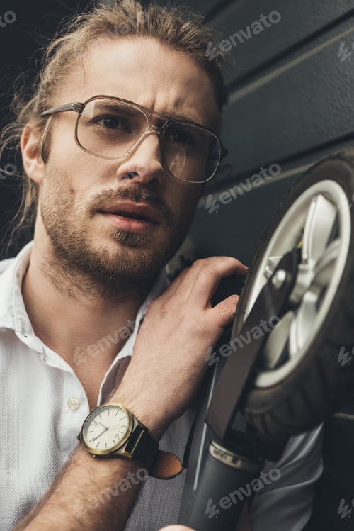 Preview: Close-up portrait of handsome stylish young man in eyeglasses holding scooter