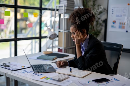 Preview: A woman in a business suit is sitting at a desk with a laptop and a notebook