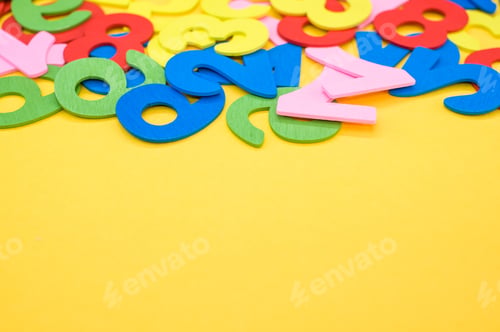 Preview: Closeup shot of the colorful wooden numbers scattered on a yellow surface - space for text