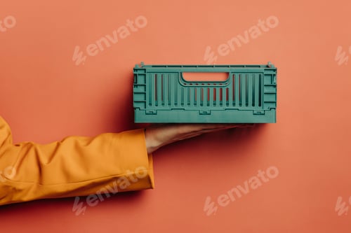 Preview: woman's hand in a yellow blazer holds a stylish pink plastic box against a pink background