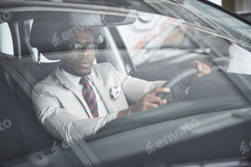 Preview: front view of Handsome african elegant serious business man drives a car