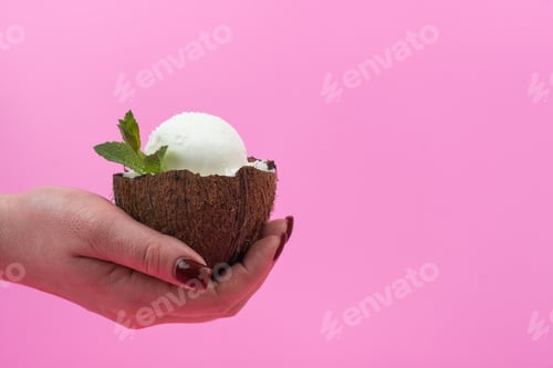 Preview: Vanilla ice cream balls in fresh coconut halves decorated with mint leaves on a pink background