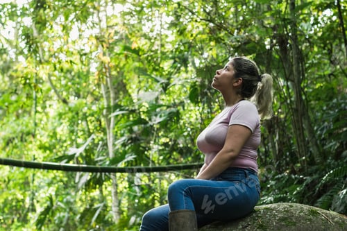 Preview: beautiful latin girl sitting on a rock in the middle of the jungle observing and admiring