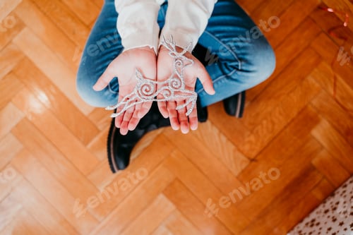 Preview: kid girl decorating christmas tree at home. holding a golden snow flake. Christmas concept