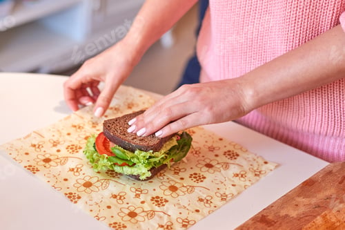 Preview: Woman hands wrapping a healthy sandwich in beeswax food wrap