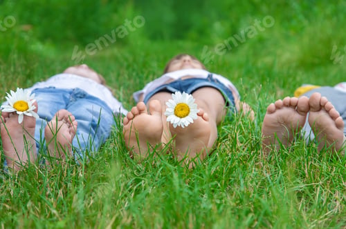 Preview: Children's feet with chamomile on green grass. Selective focus.