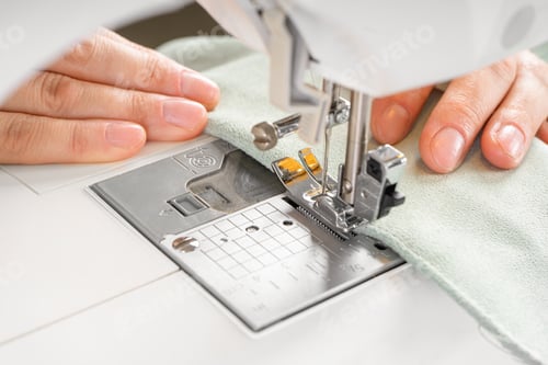 Preview: Female hands stitching white fabric on modern sewing machine at workplace in atelier