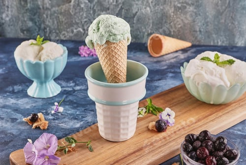 Preview: Still life with pistachio and creamy ice cream in vases and cone on blue background