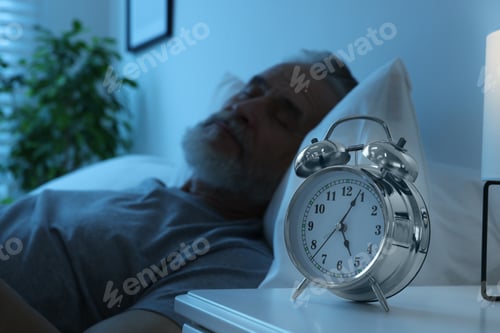 Preview: Senior man sleeping in bed at home, focus on alarm clock. Space for text