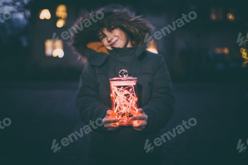 Preview: Boy with christmas lights in glass standing outdoors on street with winter coat and christmas lights