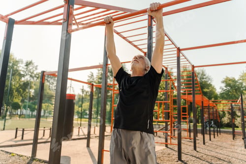 Preview: Senior man doing pull ups on horizontal bar in outdoor gym