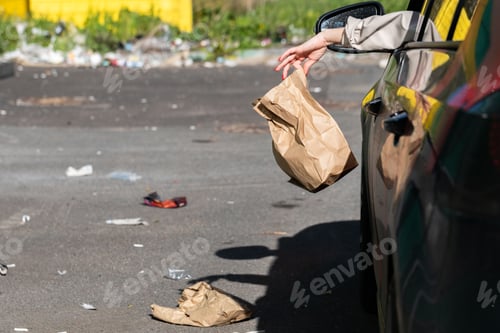 Preview: Woman holding trash paper bag in hand, out of window driving in car.