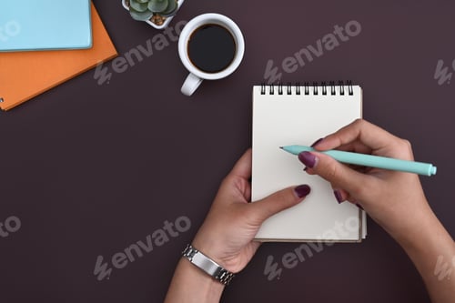 Preview: Above view stylish woman holding pen writing on empty notepad.