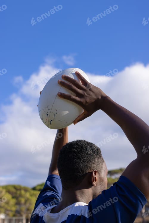 Preview: African American young male athlete holding a rugby ball, ready to throw, copy space