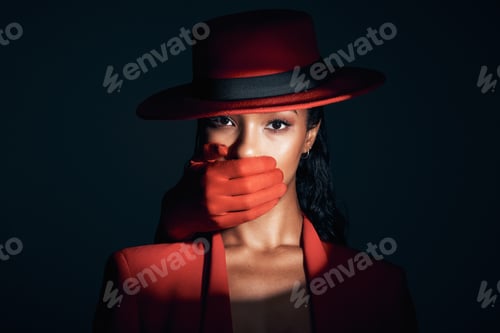 Preview: Fashion, spotlight and hand over mouth for secret and power of strong woman portrait in dark studio